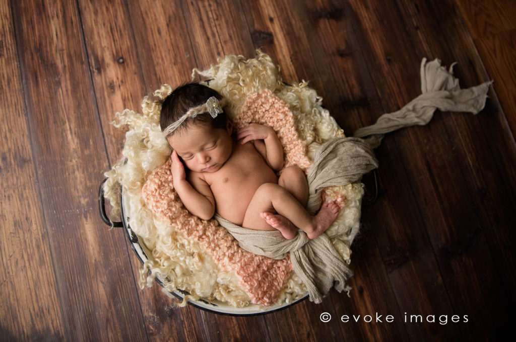 newborn baby girl in a bowl neutral color wool curls